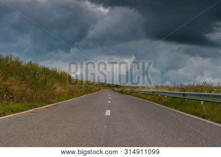 Empty Rural Asphalt Road With Green Vegetation, Dark Dramatic Gathering Stormclouds On The Sky.