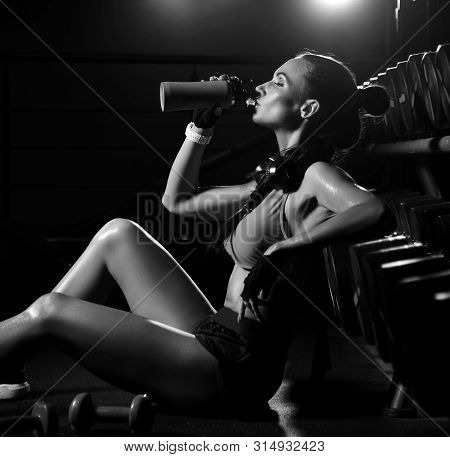 Young Athletic Woman Sits On The Floor And Drinks From Her Bottle Has A Break From Training Working 