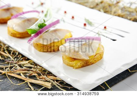Herring Canape with Potato and Onion on Natural Rustic Background. Beautiful Creative Sea Food Design of Fish Fillet with Scallions on Dry Hay and Black Slate