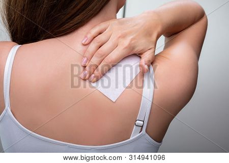 Rear View Of Woman Sticking Patch To Help With Stiff Neck