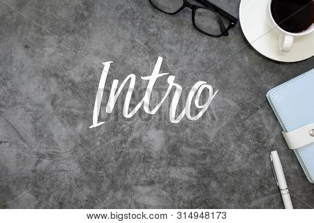 Top View Of Sunglasses, A Cup Of Coffee, Notebook And Pen On Grey Floor Background Written With Intr