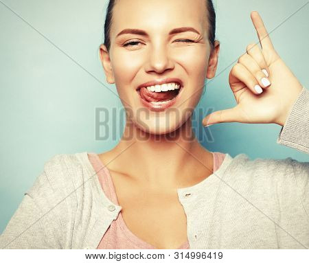 funny girl showing her tongue while posing against studio background. Emotional positive young female making faces