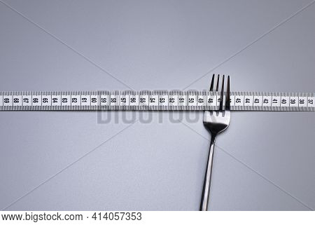 Measuring Tape And Fork On The Grey Background. The Concept Of Healthy Food And Diet. Copy Space.