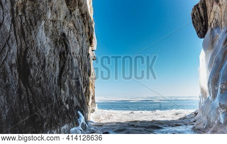 A Snow-covered Path Runs Between Two Rocks With Icy Steep Slopes. Ahead Is Lake Baikal, Covered With