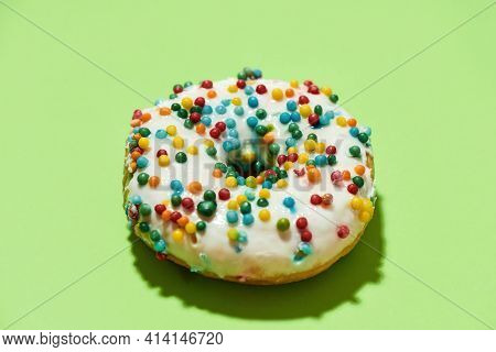 Mmm, So Delicious. Close Up Of Freshly Baked Round Glazed Donut With Colorful Sprinkles On Green Bac