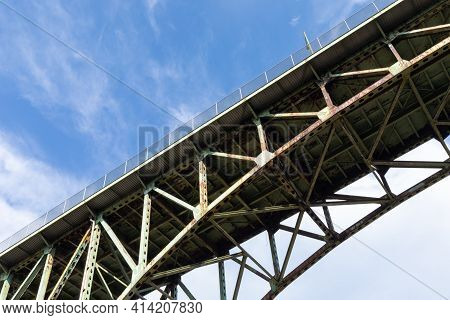 Rusted Underside Of An Arch Bridge, Decaying Infrastructure, Blue Sky With Clouds, Horizontal Aspect