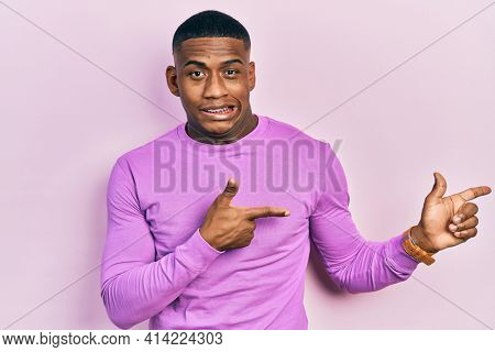 Young black man wearing casual pink sweater pointing aside worried and nervous with both hands, concerned and surprised expression 