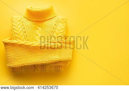 A Yellow Knitted Sweater Is Rolled Up On A Yellow Background, Copyspace. Warm Seasonal Clothing For 