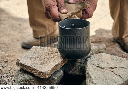 Hands Of An Adult Man Pouring Hot Coffee From A Turk Into A Metal Mug
