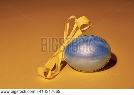 Pearl Colored Egg With Yellow Ribbon On A Yellow Background. Easter Concept.