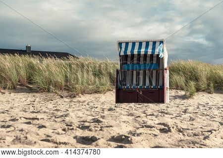 Landscape With A Single Decked Chair On The Beach And Marram Grass Under A Dramatic Sky. Summer Scen