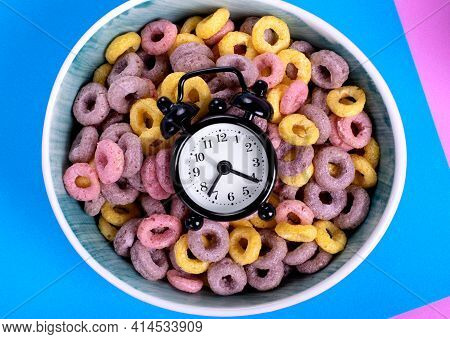 Alarm Clock On Top Of Multicolored Fruit Loops With Natural Colorants In The Ceramic Bowl. Breakfast