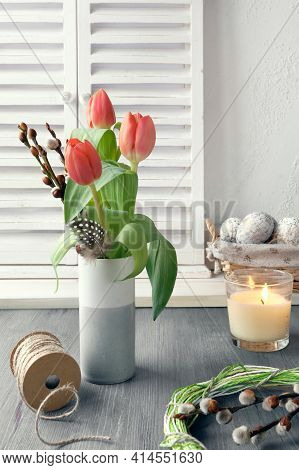 Springtime Easter Decorations On Rustic Wooden Table. Candle In Glass. Easter Eggs In Basket, Quail 