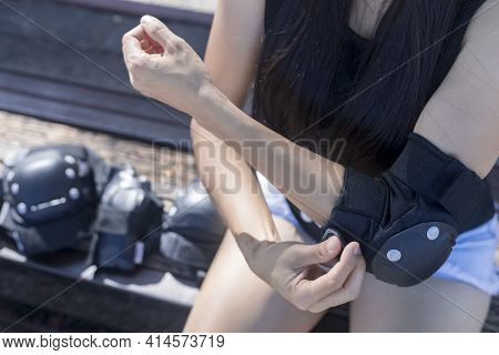 Close Up Woman Surf Skate Board Putting On Elbow Protector Pads On Her Arm And Wearing Wrist Guards.