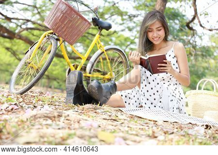An Asian Girl Enjoying Reading In The Garden. A Female Office Worker Enjoying Time Away From Technol