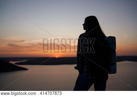 Silhouette Of Young Woman Standing On Edge Of Rock And Looking At Summer Sunset Over Dniester River.