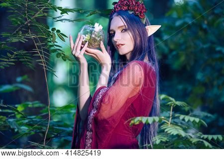 Portrait Of Caucasian Girl With Artistic Elf Ears And Flowery Garland Holding Glass Dome With Ground