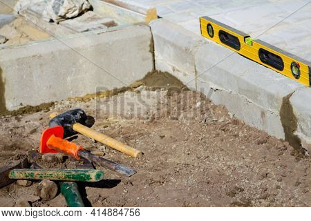Defocus Paving Garden. Yellow Spirit Level, Hammer, Mallet, Chisel Lie On The Ground. Set Of Tools F
