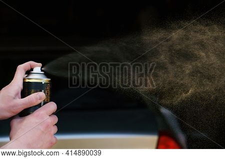A Man Sprays Paint From A Can In Front Of A Car