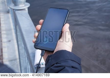 A Man Charges A Smartphone With A Power Bank. The Phone In Hand Is Being Charged With A Portable Cha