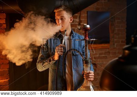 Young man blows smoke in hookah bar, hooka