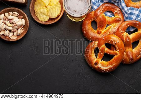 Lager beer mug, nuts, potato chips and fresh baked homemade pretzel with sea salt on stone table. Classic beer snack. Top view flat lay with copy space