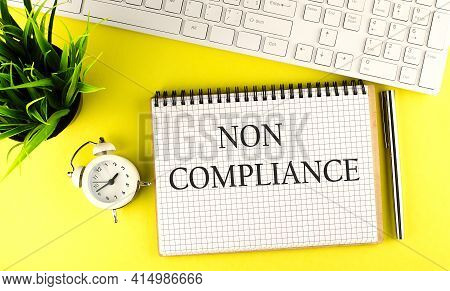 Non Compliance Text On Notebook With Keyboard , Pen And Alarm Clock On Yellow Background