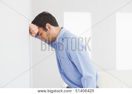 Sad man with fist clenched leaning his head against a wall