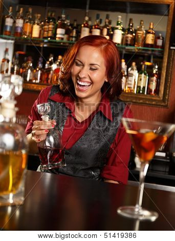 Beautiful redhead barmaid with bottle behind bar counter 