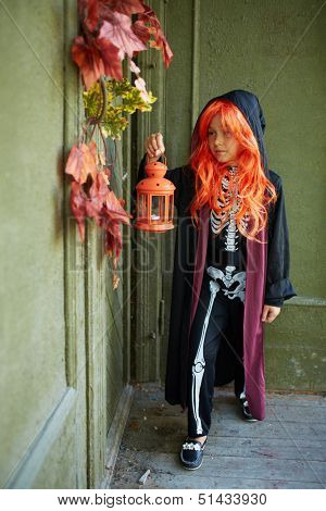 Portrait of Halloween girl with lantern standing by the door of dilapidated house