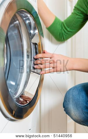 Young woman or housekeeper has a laundry day at home, she takes the laundry or whites out of your washing machine or the dryer