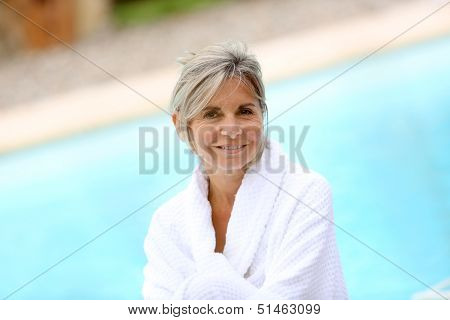 Portrait of smiling senior woman sitting by resort pool
