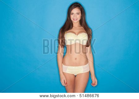 Sexy woman with a lovely body standing posing in yellow lingerie and twiddling her long brunette hair in her fingers, three quarter studio portrait
