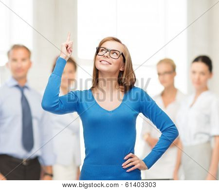 advertisement concept - attractive young woman in casual clothes and black eyeglasses pointing her finger up