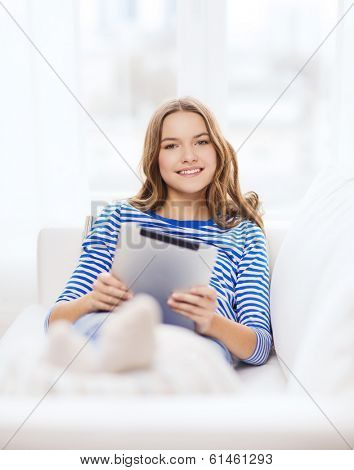 home, technology and internet concept - smiling teenge girl lying on the couch with tablet pc computer at home