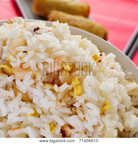 closeup of a bowl with appetizing chinese fried rice and some springrolls in a plate on a set table