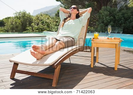 Beautiful young woman relaxing by swimming pool with breakfast on table