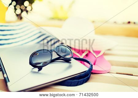 beach, summer, vacation, accessories and technology concept - close up of laptop and summer accessories on beach