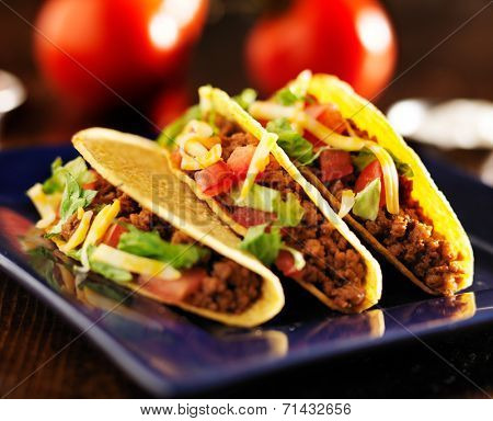 three beef tacos with cheese, lettuce and tomatoes