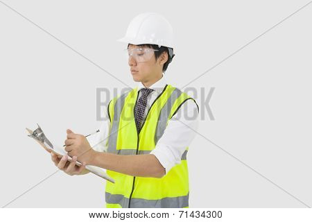 Man in reflector vest and hard hat writing on clipboard in office