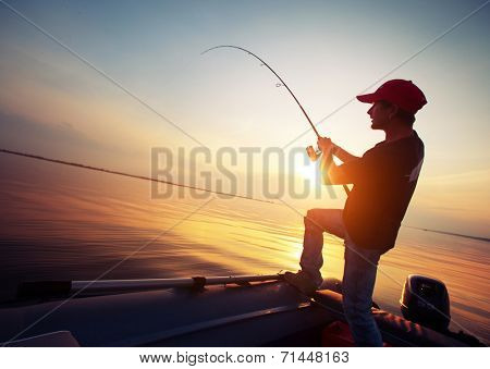 Young man fishing from the boat at sunset