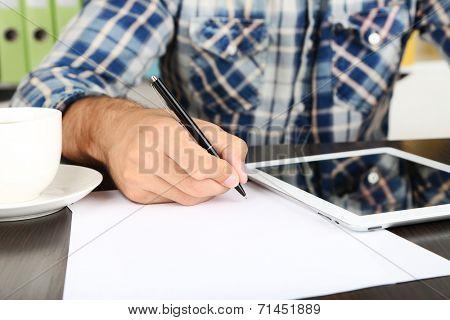 Man sitting on wooden table and working on tablet closeup