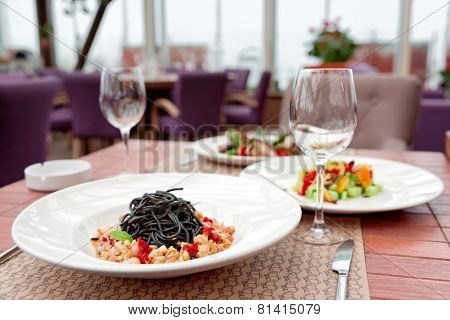 Black squid ink pasta with seafood and other dishes on restaurant table