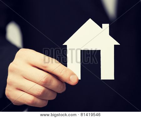 closeup pisture of man in suit holding paper house