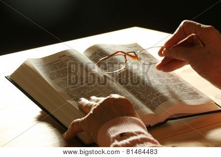 Hands of old woman with Bible on table and dark background