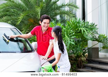 Asian couple cleaning windscreen or windshield and headlamps while car wash 