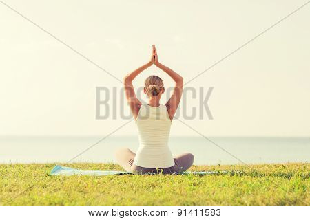 fitness, sport, people and lifestyle concept - of woman making yoga exercises on mat outdoors from back
