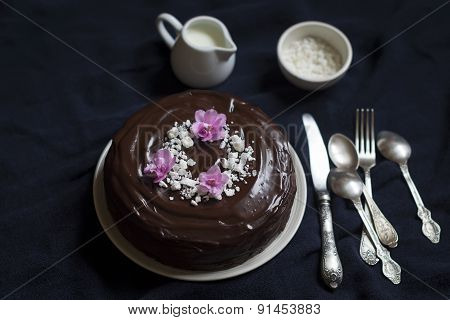 Chocolate Cake Decorated With Meringue Crumbs And Violets On A Dark Surface