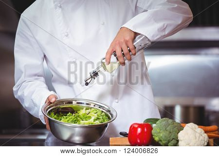 Chef putting oil on salad in commercial kitchen