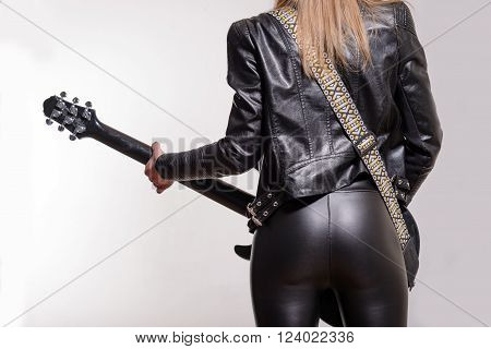 Photo of the back of a female guitar player in leather jacket and trousers standing and playing on white background.